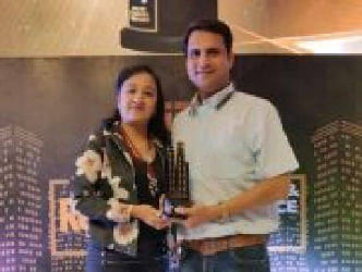 Man and woman smiling while holding an award trophy at a real estate-themed event backdrop.